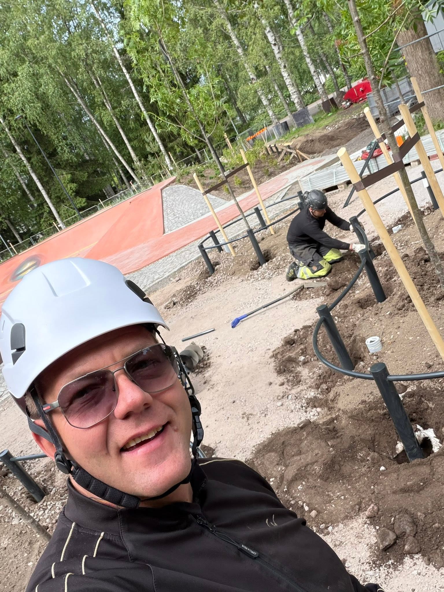 Workers on an outdoor construction site, with a worker wearing a helmet and safety glasses in the foreground.